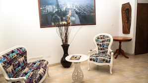 Une pièce décorée d’un tableau représentant un paysage urbain, d’un canapé à motifs, d’une petite table ronde et d’un objet décoratif en bois accroché au mur.