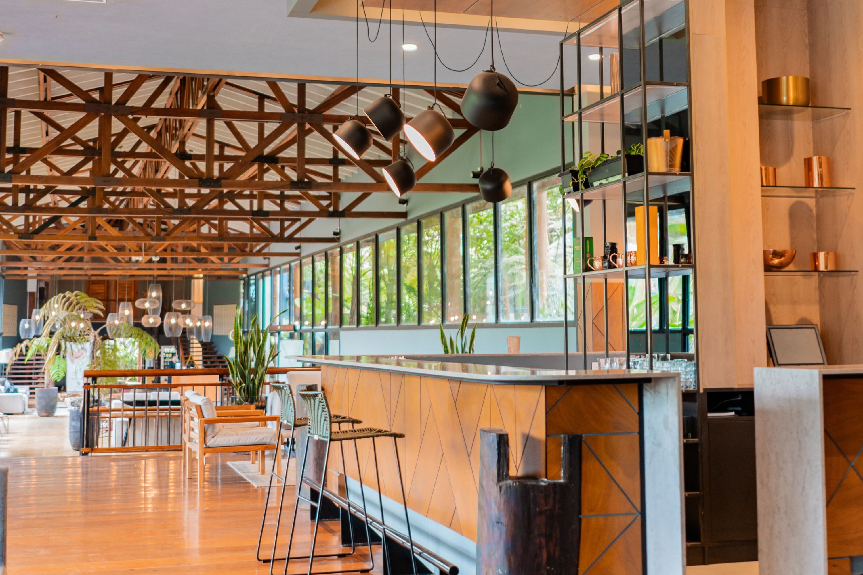 Un área de bar amplia con suelo de madera, una barra larga y lámparas colgantes.