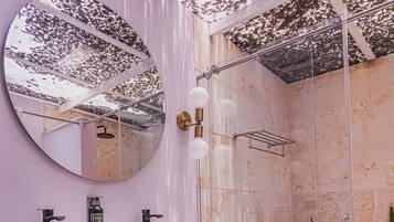A bathroom with a stone sink, a large mirror, a shower, and a plant.