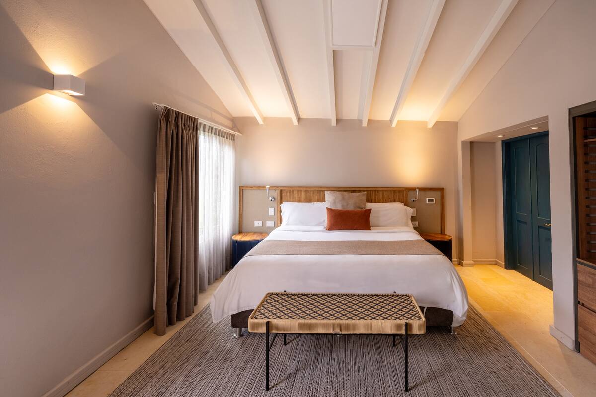 Ein Hotelzimmer mit einem großen Bett, Nachttischen, einer Bank und einer Decke mit freiliegenden Balken.