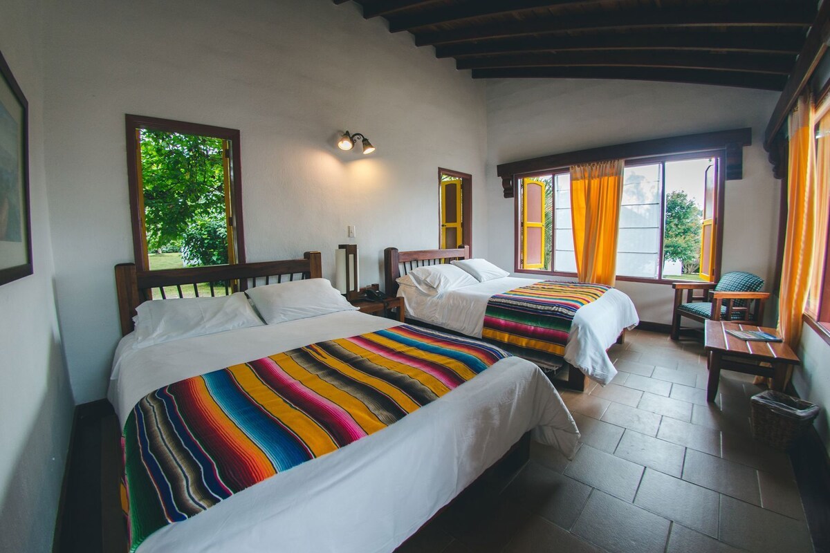 A room with two beds, a small table, and a window with curtains.