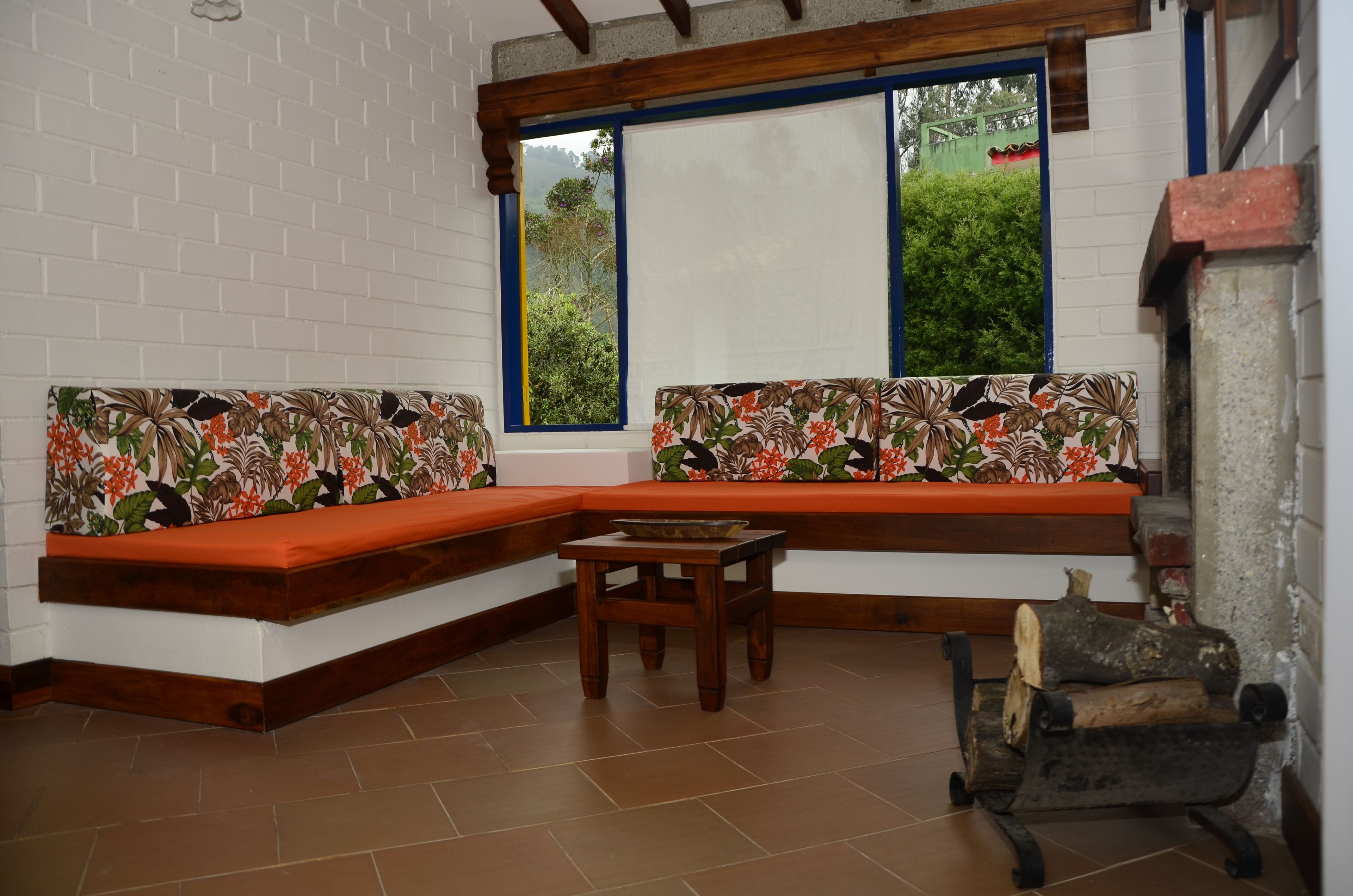 A corner seating area with a bench and a small table, a window with a view of greenery, and a rustic log bench.