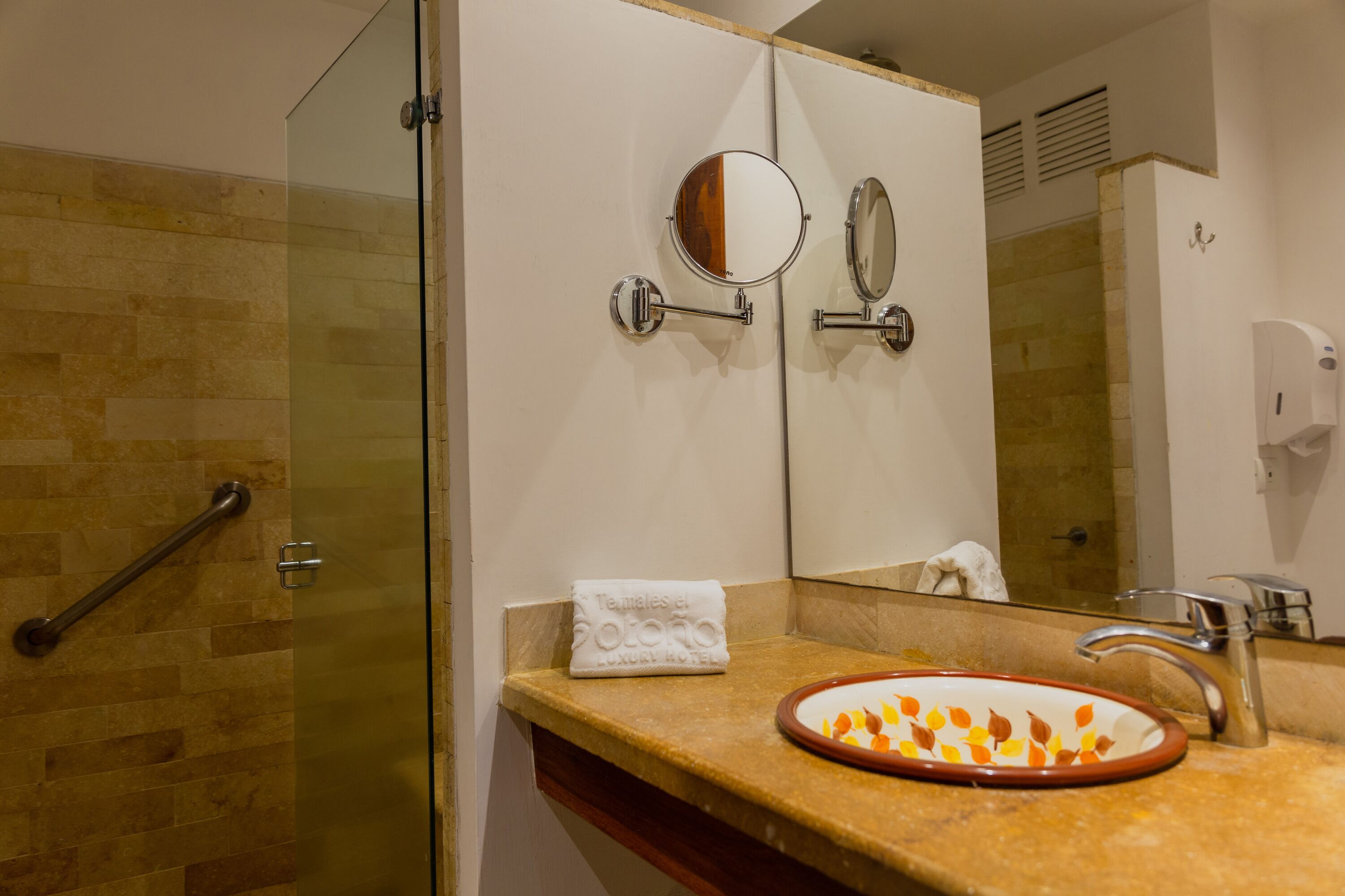 A bathroom with a glass shower enclosure, a sink with a decorative bowl, a towel, and a mirror.