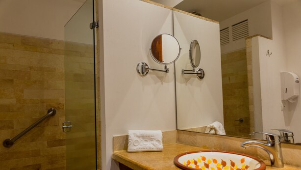 A bathroom with a glass shower enclosure, a sink with a decorative bowl, a towel, and a mirror.