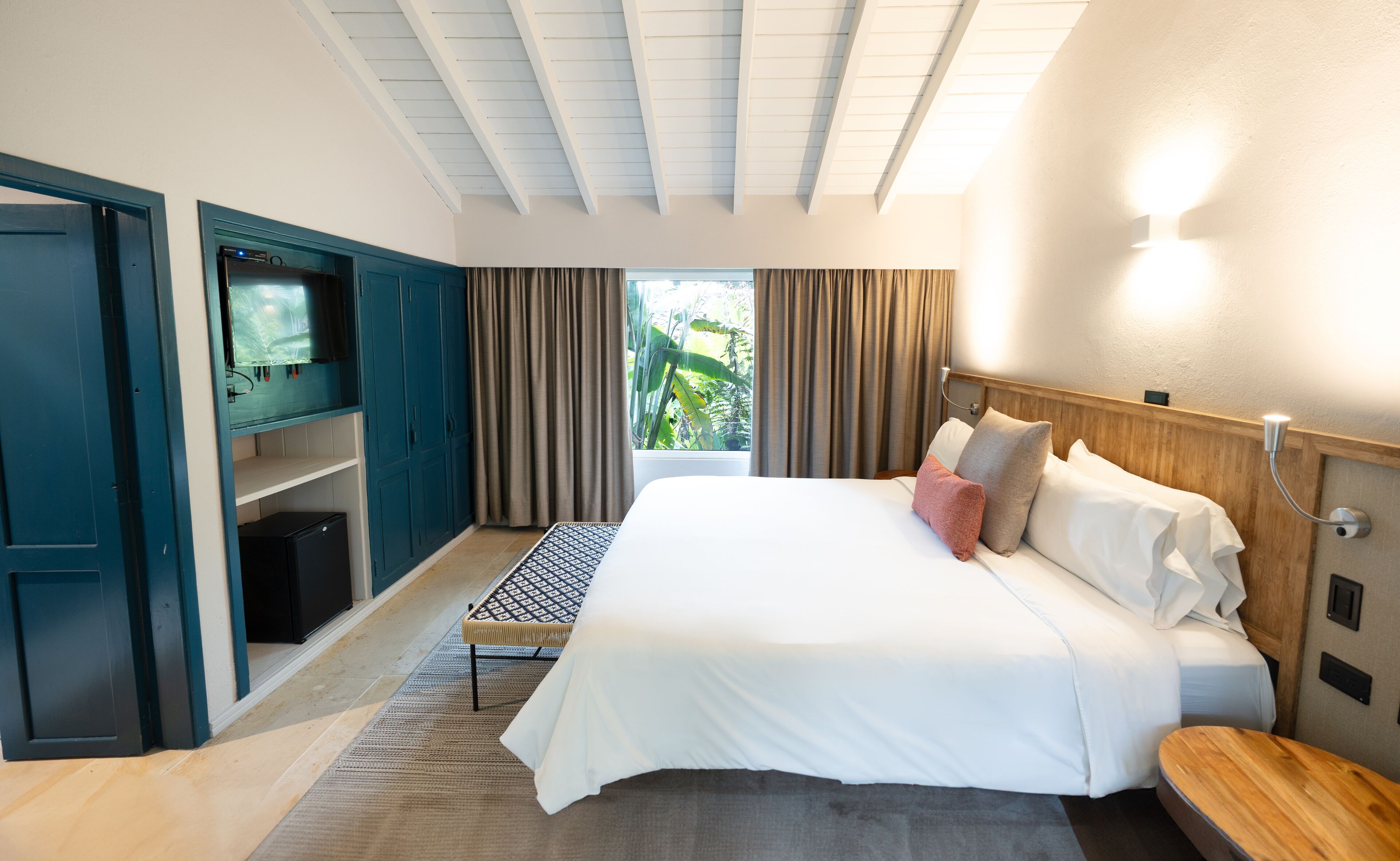 Une chambre d’hôtel avec un lit, une télévision, une armoire en bois et une fenêtre avec des rideaux.
