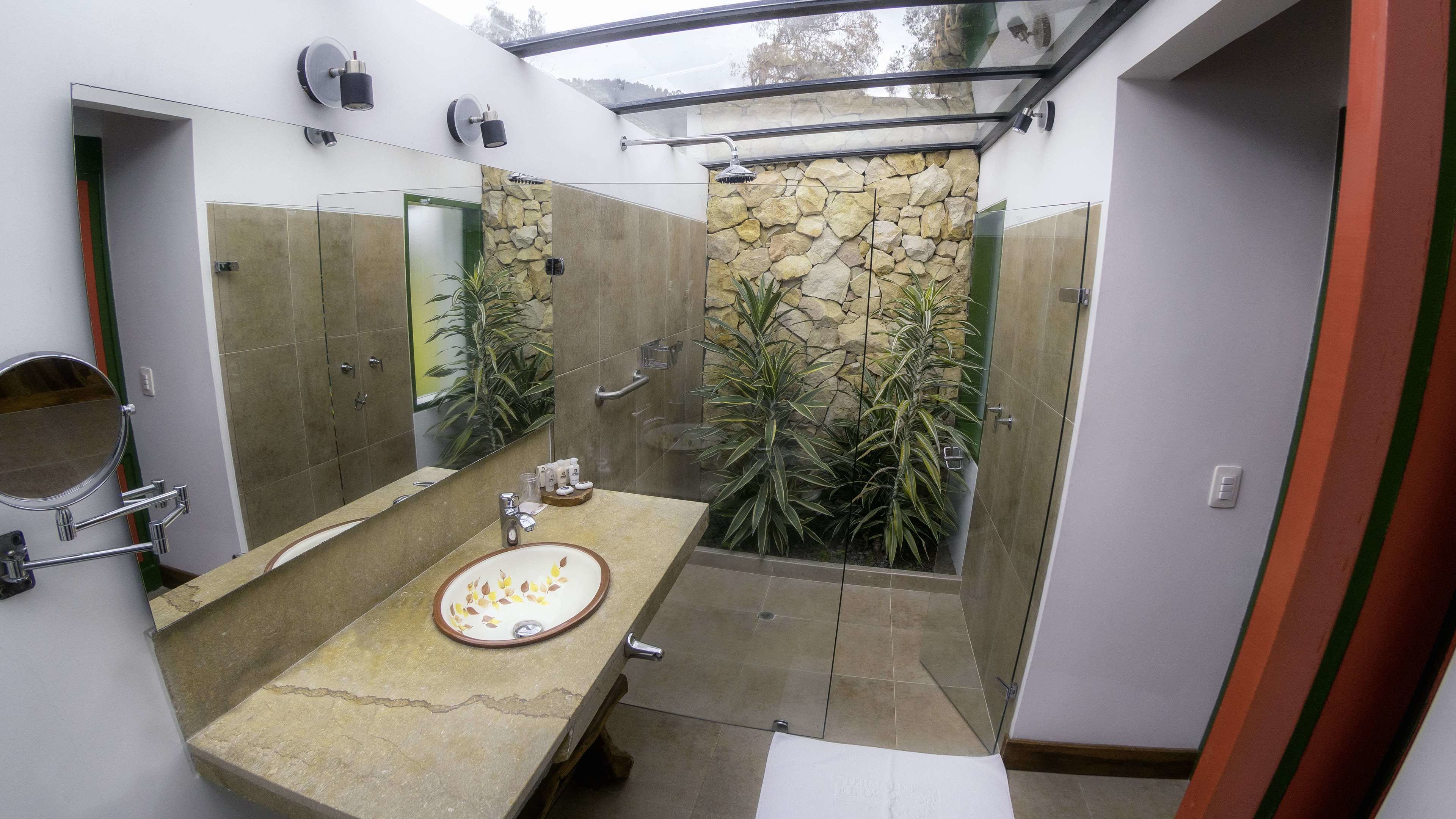 Une salle de bain moderne avec un mur d’accent en pierre, un grand miroir et une douche séparée par des parois en verre.