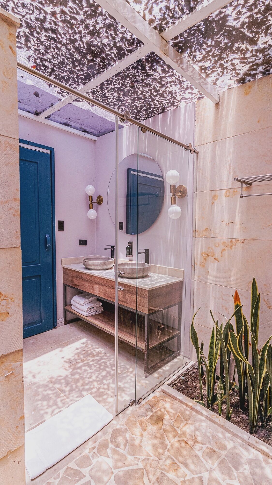 A bathroom with a glass shower enclosure, a blue door, and a large mirror.