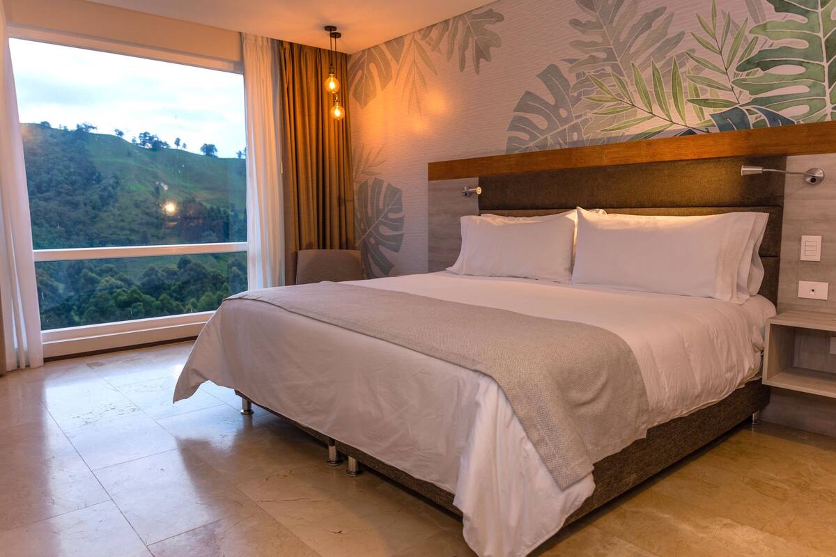 Ein Hotelzimmer mit einem großen Bett, Blick auf eine grüne Landschaft und einem Holzkopfteil.