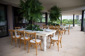 An outdoor dining area with wooden chairs and tables, surrounded by large potted plants. - Termales del Otoño (Villamaria)