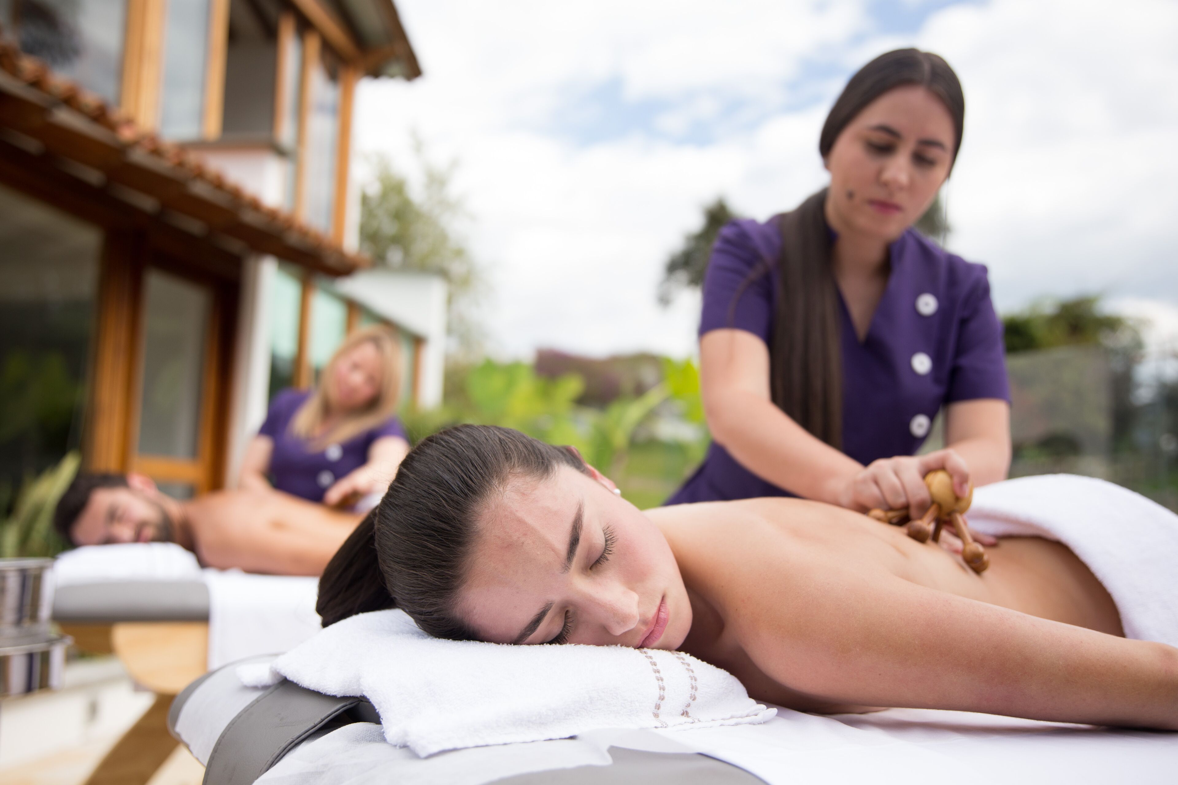 A massage therapy session in a spa setting with a wooden exterior and a view of greenery.