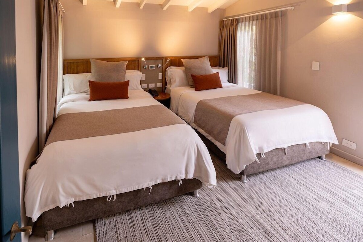 A hotel room with two beds, a wooden headboard, a nightstand, and a large window with curtains.