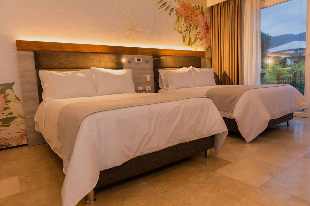 Ein Hotelzimmer mit zwei Betten, einem Holzkopfende, einer floralen Wandmalerei und Blick auf Grünfläche.