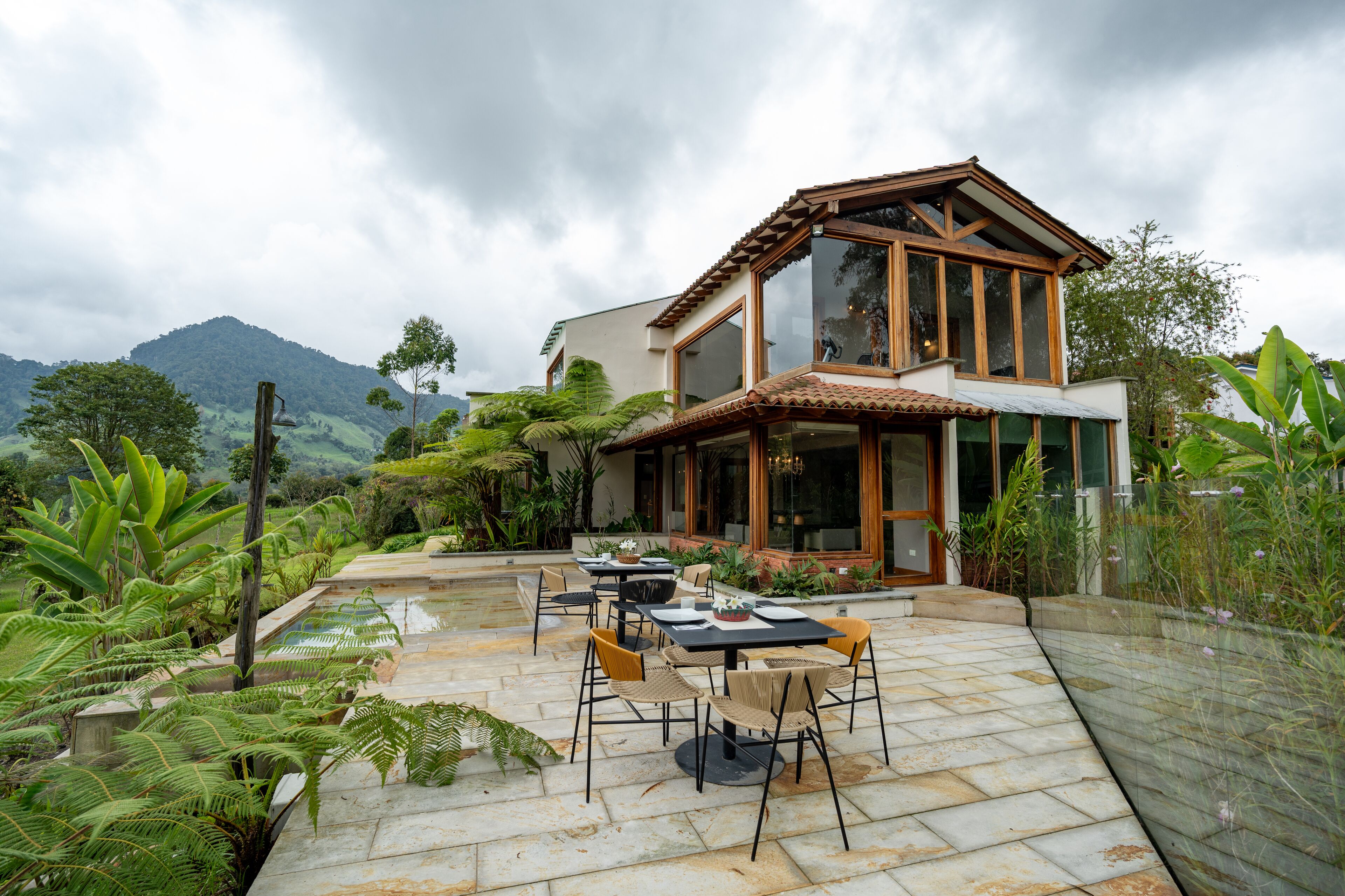 Een tweelaags huis met een patio, buitenmeubilair en weelderige beplanting.
