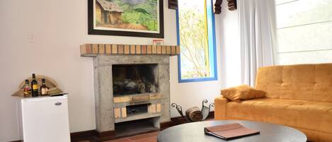 A living room with a fireplace, a sofa, a small fridge, and a window with curtains.