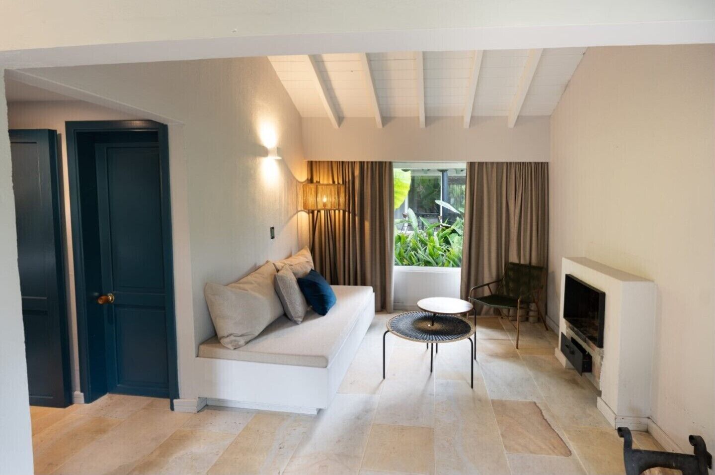 A living room with a sofa, a small round table, a fireplace, and a view of greenery outside.