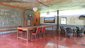 A dining area with a wooden table and red chairs, surrounded by ornate wall carvings and a large painting. - Mertha Jati Hotel & Bungalow (Kuta)