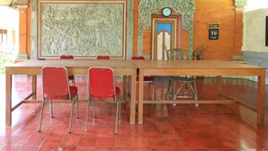 A room with a large mural, a wooden table, and red chairs. - Mertha Jati Hotel & Bungalow (Kuta)