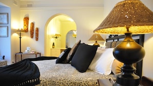 Quarto de hotel com uma cama, uma luminária, um espelho e uma mesa pequena com xícara e pires.