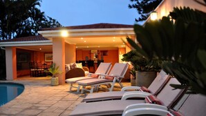 Área da piscina com espreguiçadeiras e um bar ao fundo.