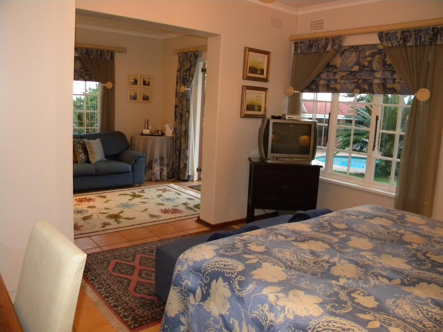 A bedroom with a bed, a television on a stand, a sofa, and a view of a swimming pool.