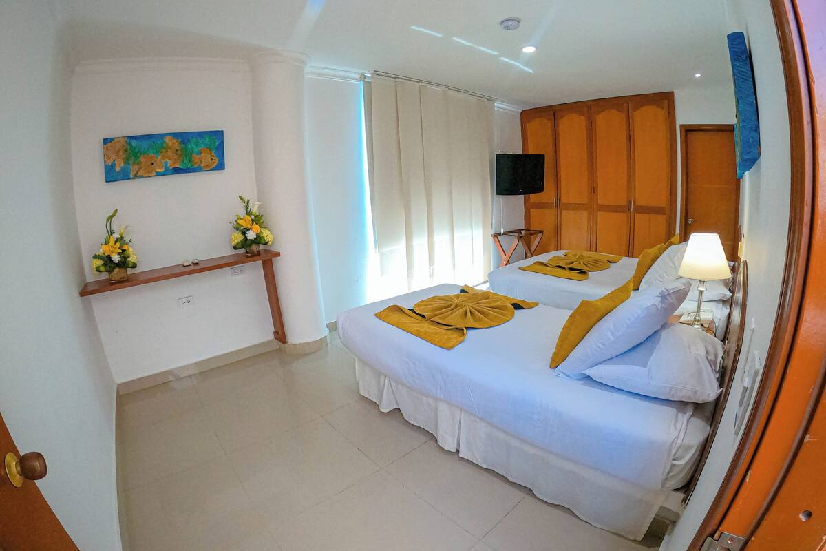 A hotel room with two beds, a TV, a desk with a lamp, and a painting on the wall.