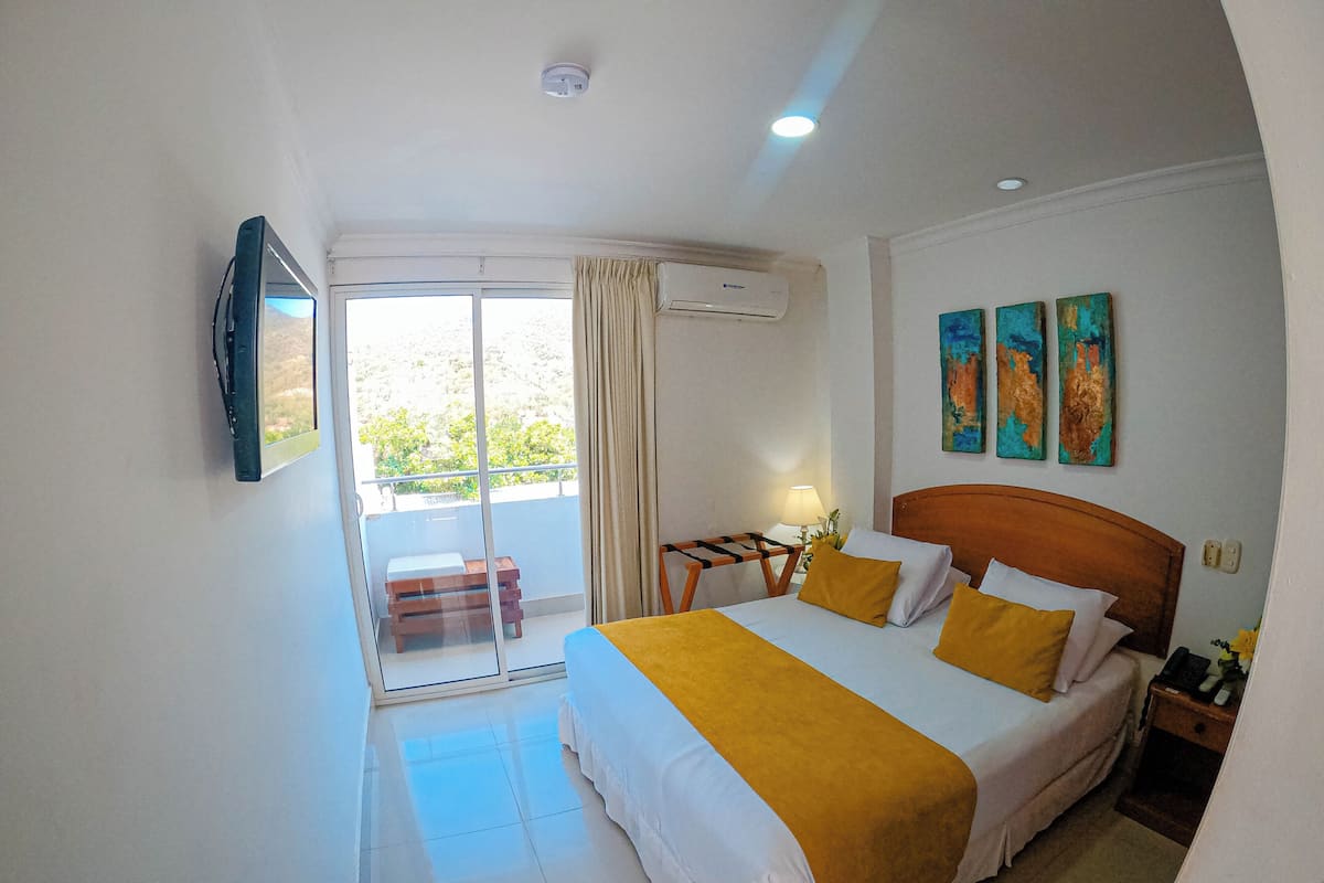 A hotel room with a bed, a desk, a chair, and a balcony.