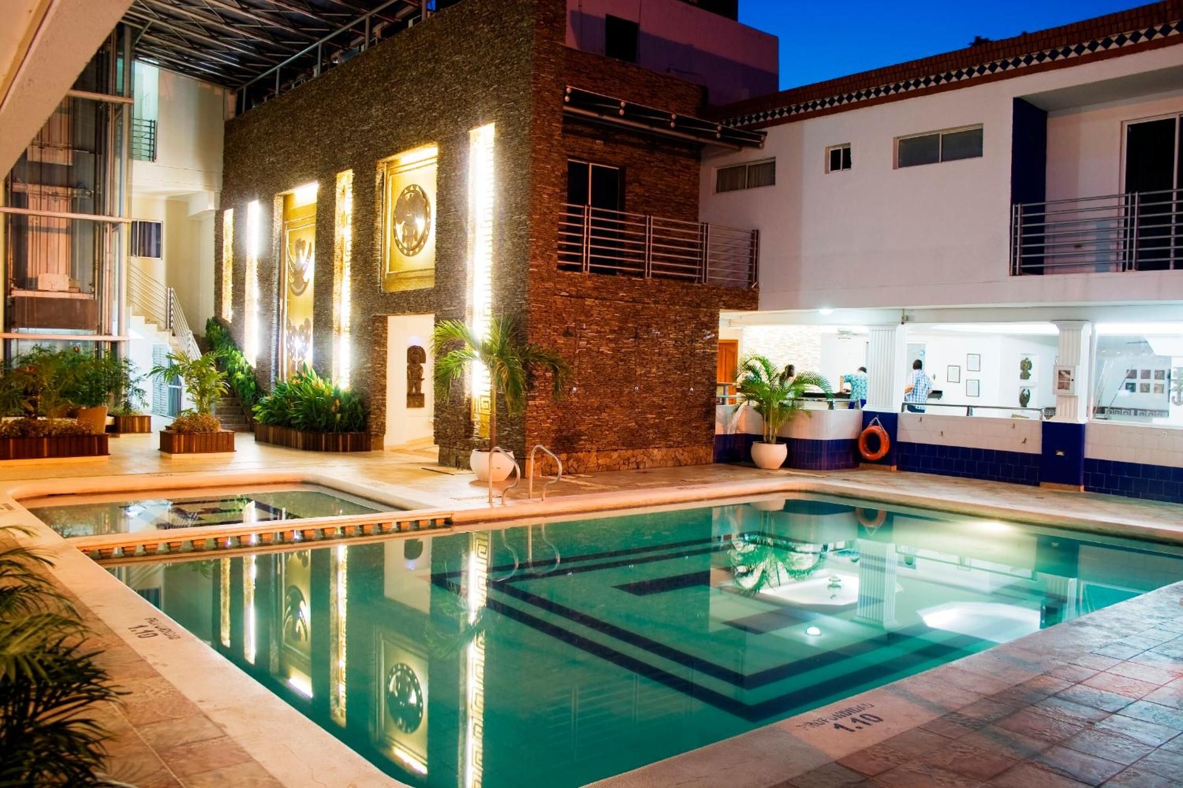 A swimming pool with a clear water surface, surrounded by a building with a brick facade and multiple windows.