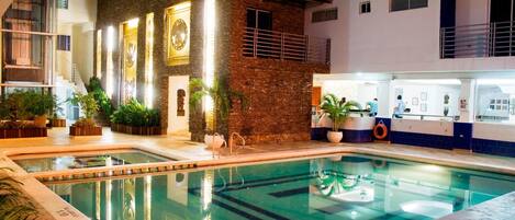 A swimming pool with a clear water surface, surrounded by a building with a brick facade and multiple windows.