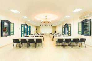 A conference room with multiple tables and chairs, a chandelier, and large windows with green shutters.