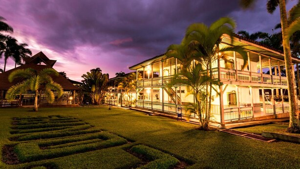 A two-story hotel with a balcony, surrounded by a well-maintained lawn and palm trees. - Decameron Las Heliconias (Quimbaya)