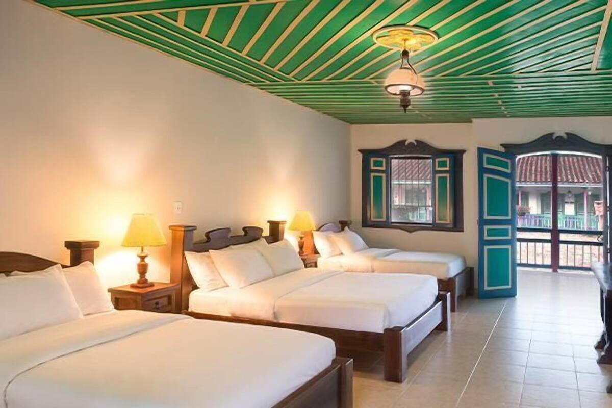 A hotel room with three beds, wooden headboards, and a tiled floor.