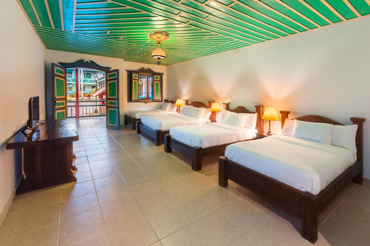 A hotel room with three beds, a desk, and a view of the outside.