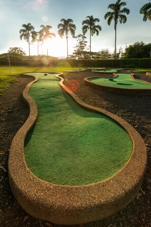 Um campo de minigolfe com percurso verde sinuoso e vários buracos.