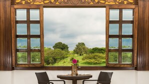 A room with a large window, two chairs, a small table, and a vase with flowers. - Decameron Las Heliconias (Quimbaya)