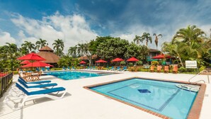 A pool area with multiple swimming pools, lounge chairs, and red umbrellas. - Decameron Las Heliconias (Quimbaya)