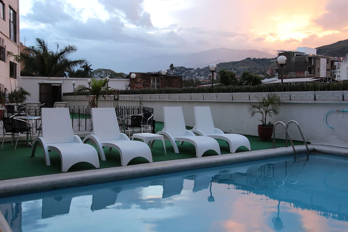 A rooftop pool area with lounge chairs and a table, surrounded by buildings and a view of the cityscape.