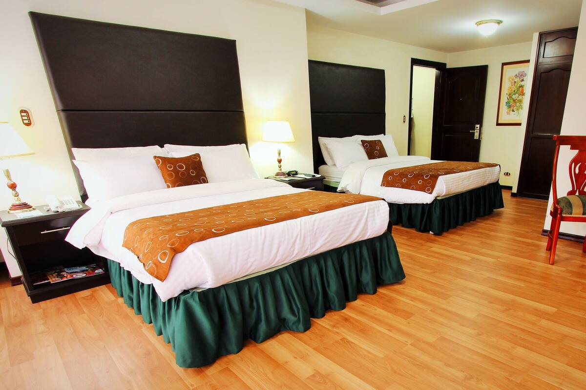 A hotel room with two beds, a desk, a chair, and a mirror.