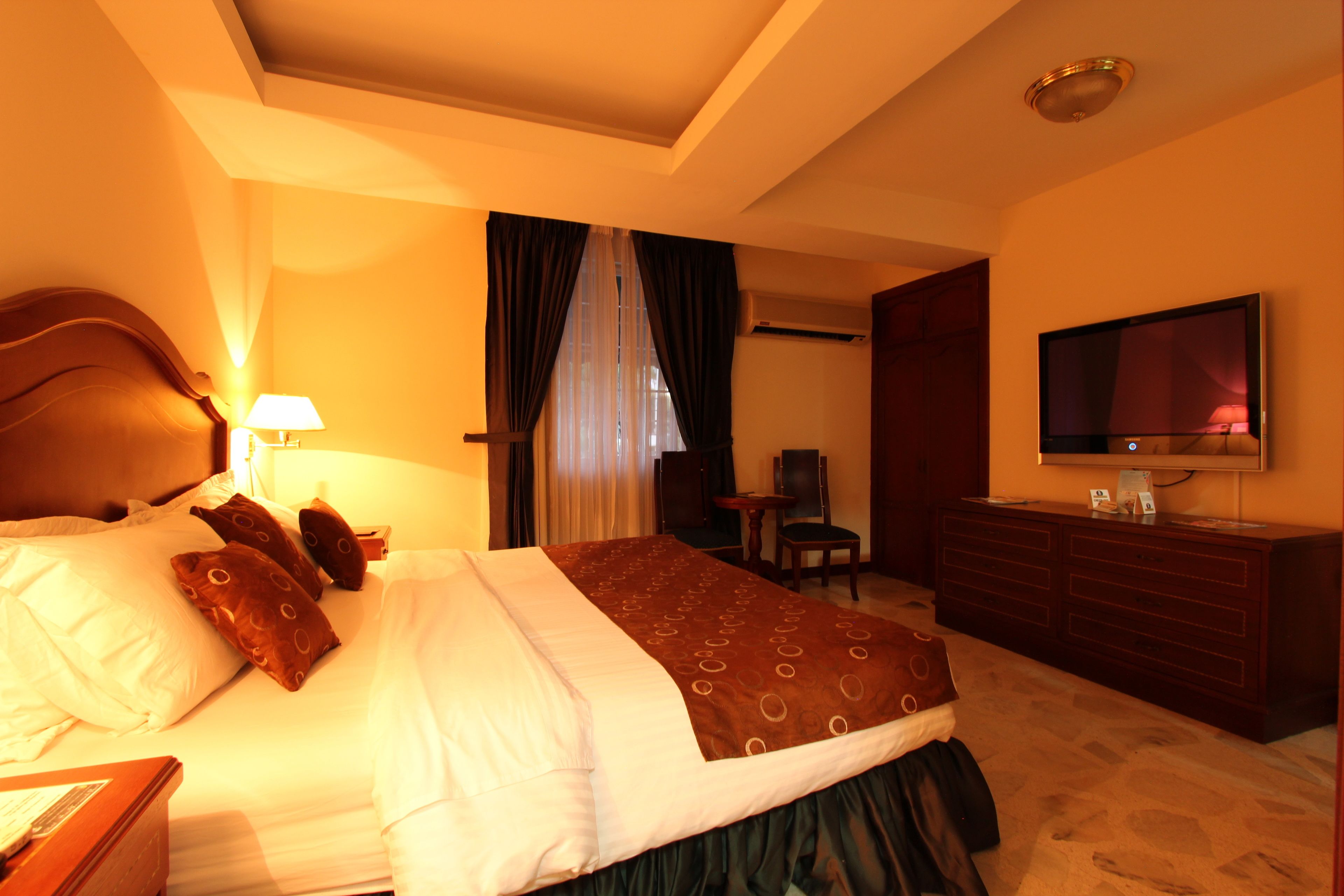 A hotel room with a bed, a desk, a chair, a TV, and a dresser.