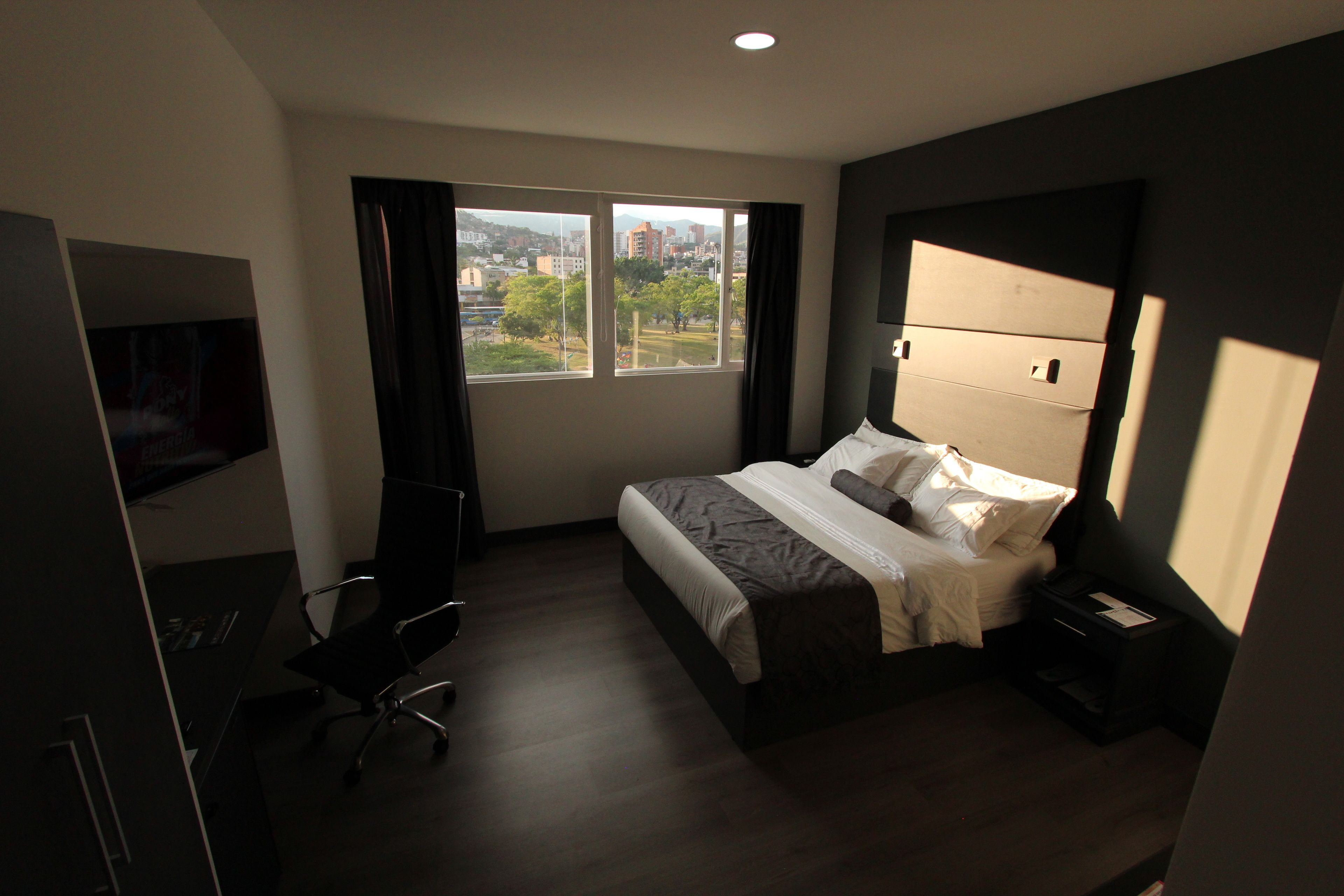 Habitación de hotel con cama, escritorio, silla, televisor y ventana con vista a la ciudad.