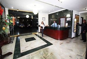 A hotel reception area with a marble floor, a reception desk, and a large plant.