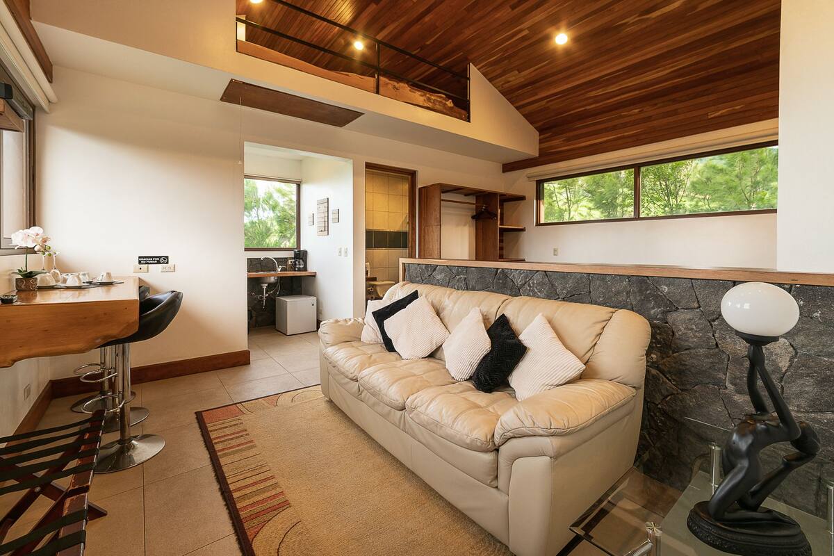 A modern living room with a beige sofa, a wooden ceiling, and a stone accent wall.