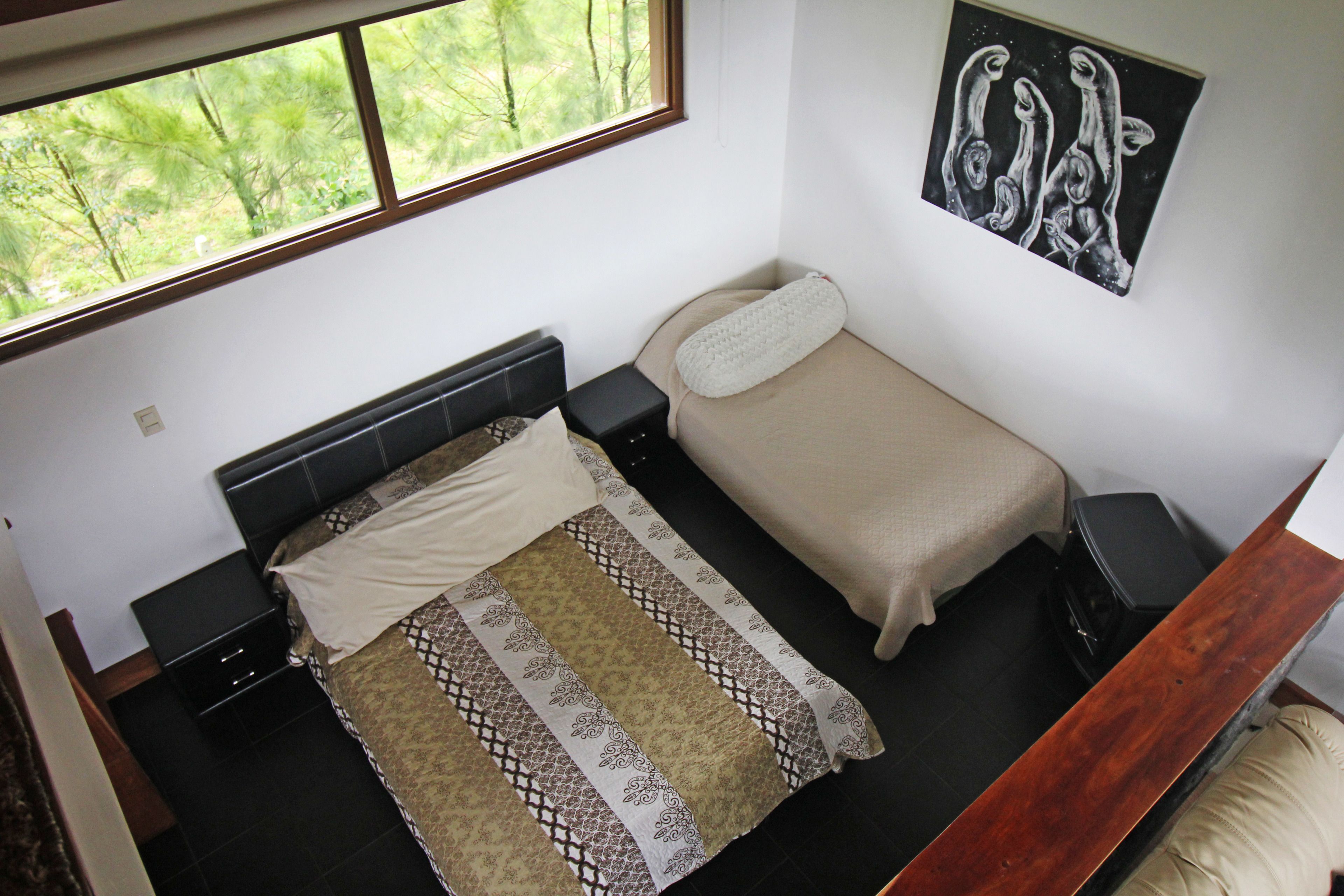 Ein Schlafzimmer mit einem Bett, einem Nachttisch, einem Fenster und einem Bild an der Wand.