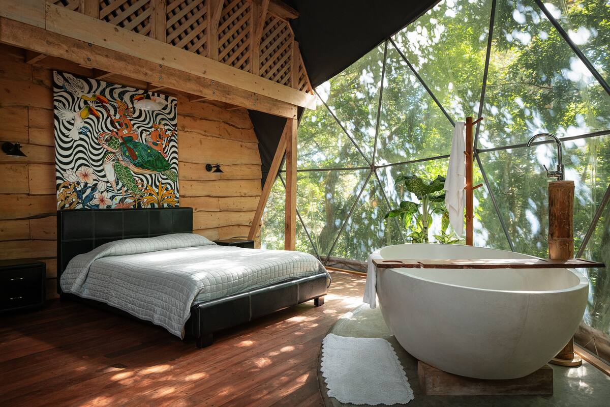 A bedroom with a bed, a large window, and a bathtub.