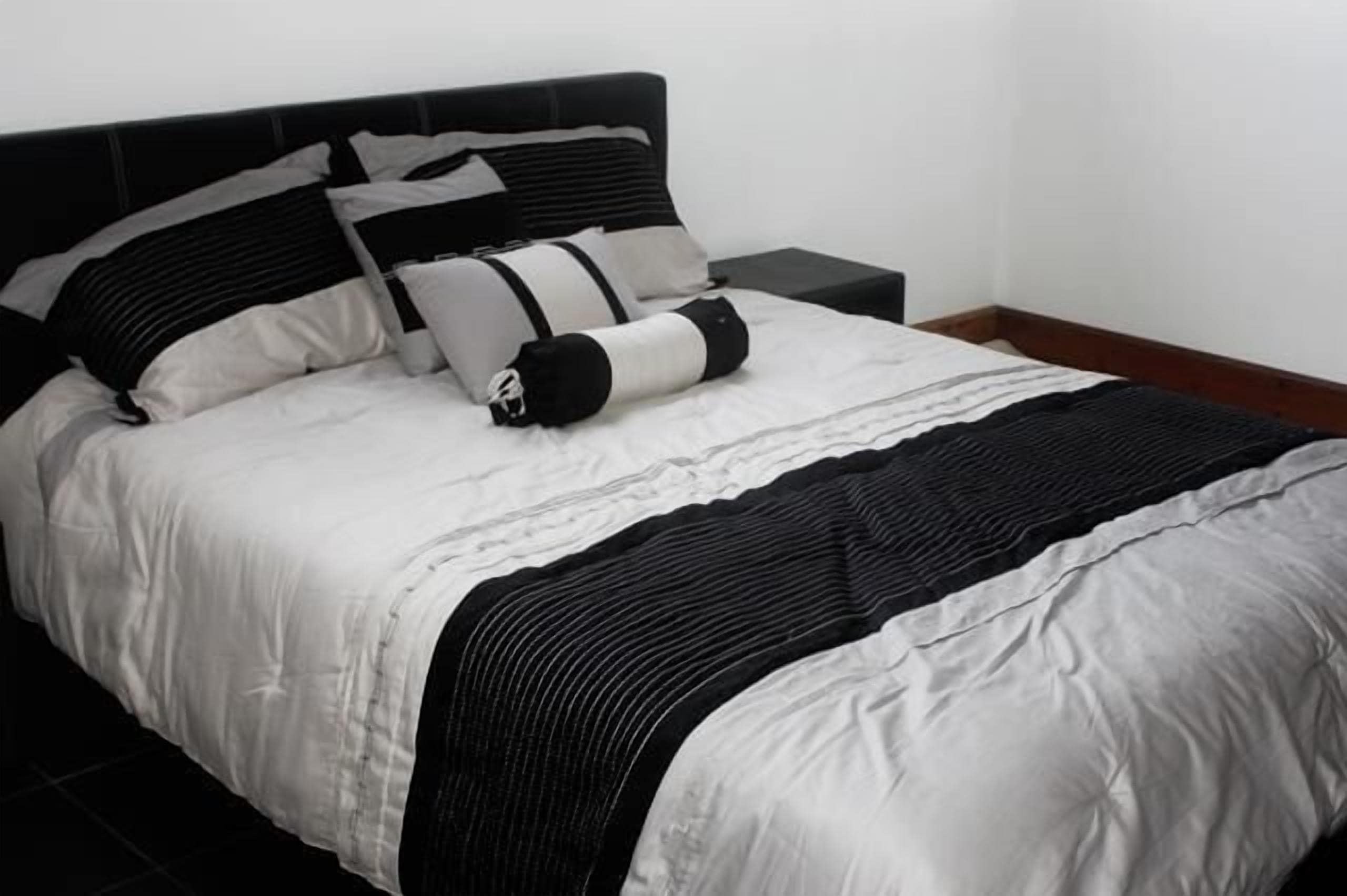 A neatly made bed with a black and white striped bedspread and pillows, a wooden headboard, and a small bedside table.