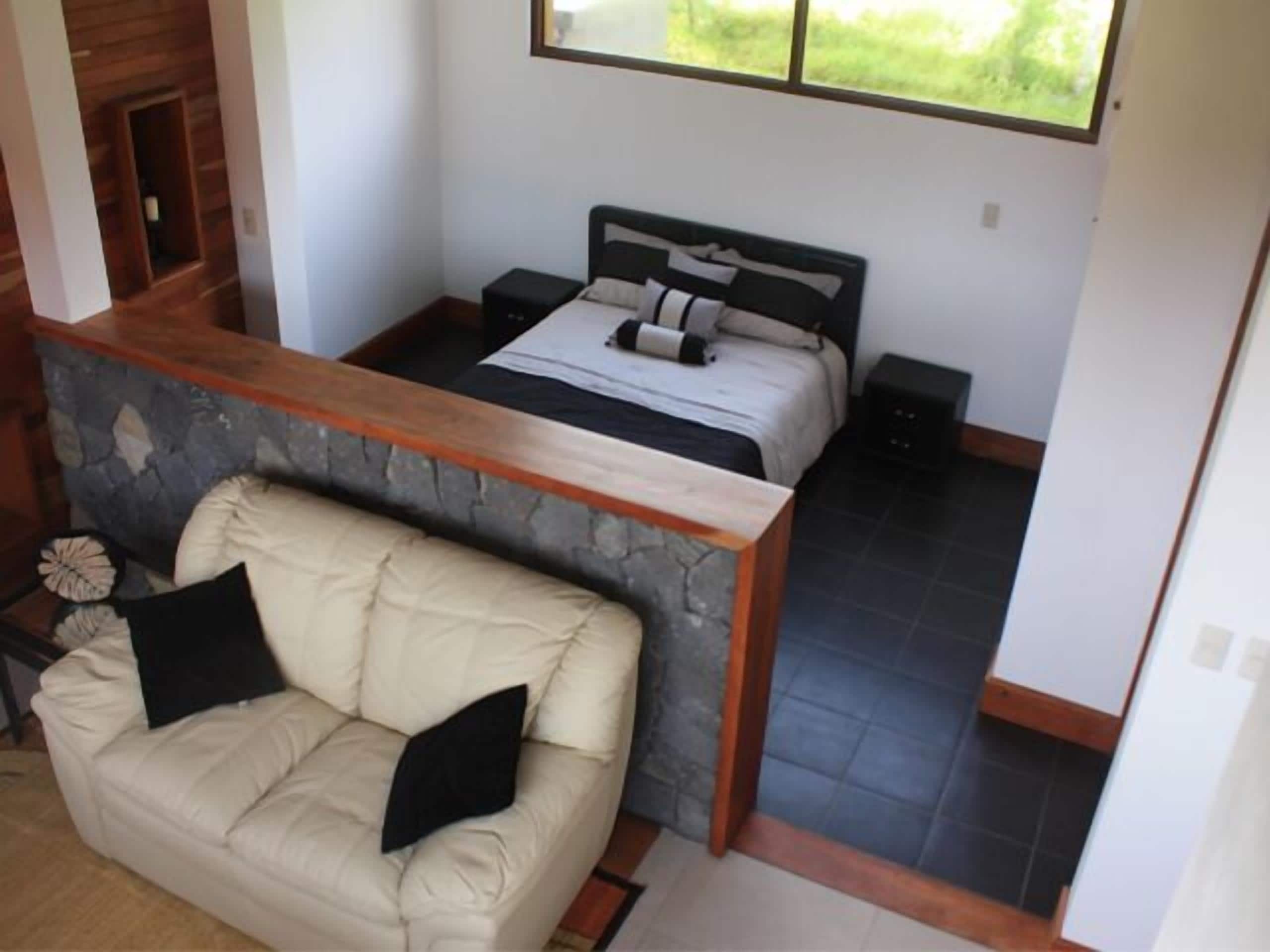 Camera da letto con parete in pietra decorativa, un letto con testiera, un comodino, una panca in legno e vista sul verde.