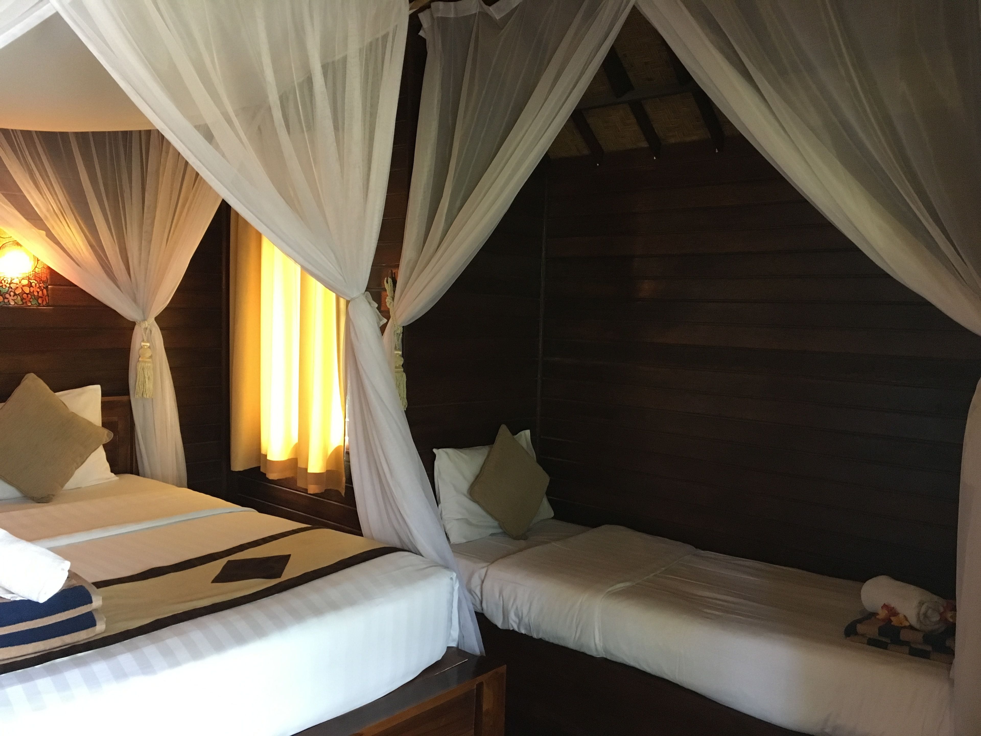 A room with two beds, each with white bedding and pillows, and a canopy bed with sheer white curtains.