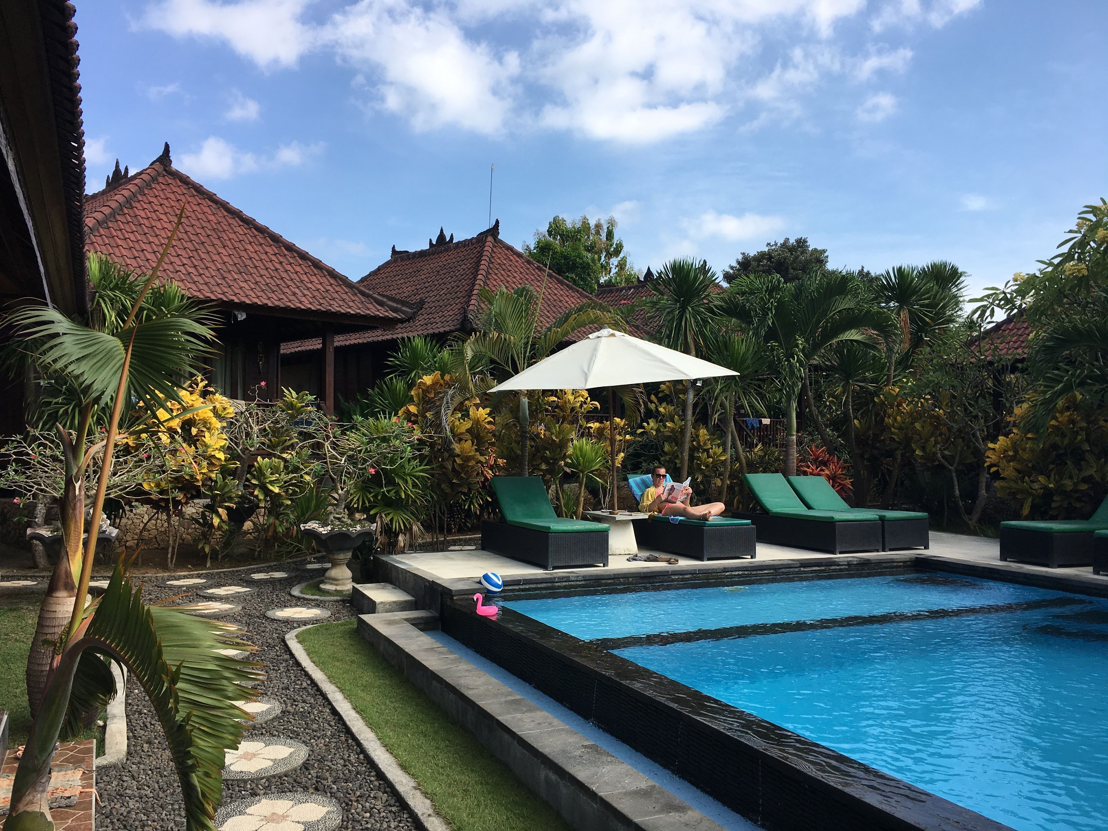 A swimming pool with lounge chairs and a person reading a book.