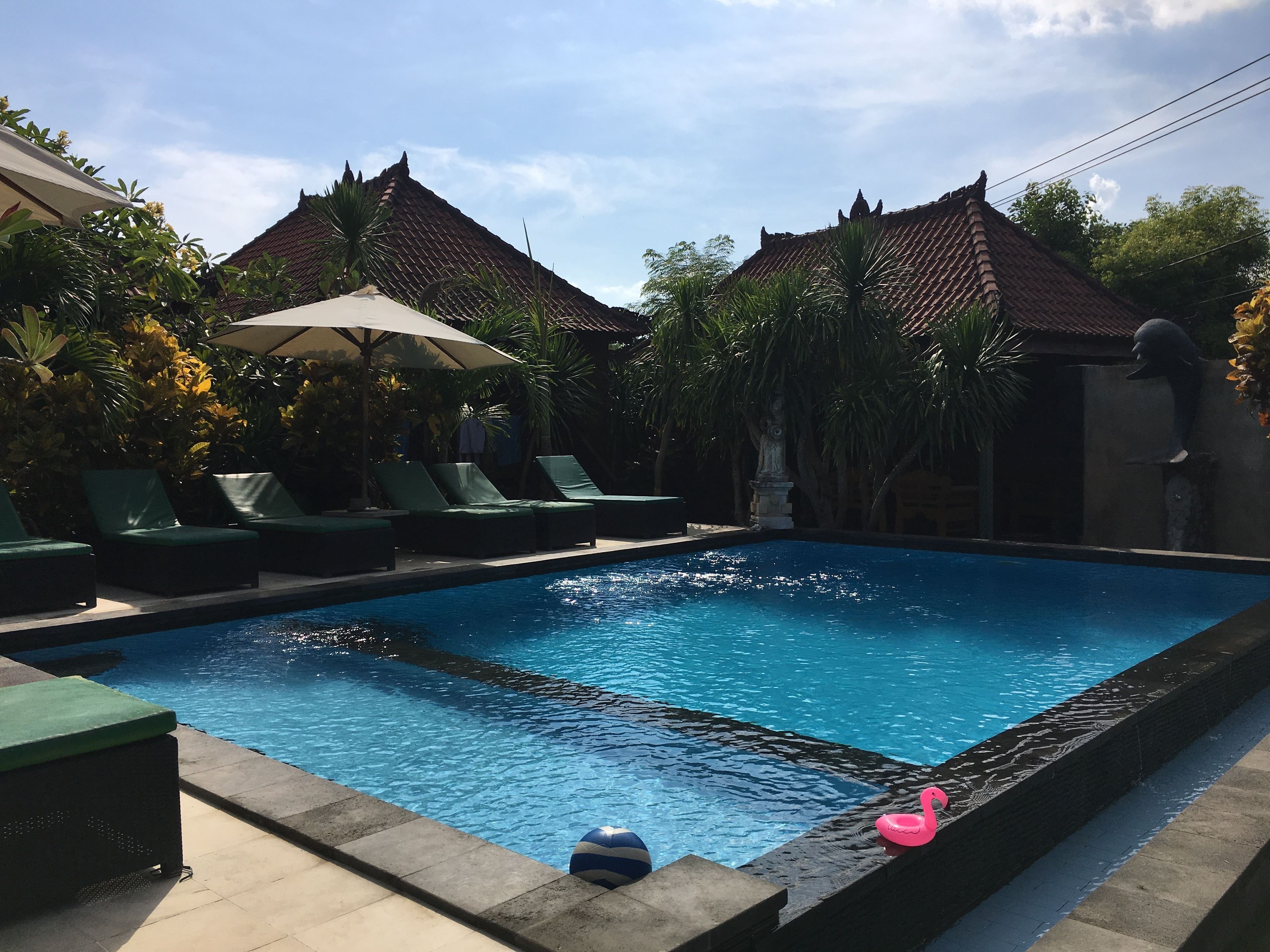 A swimming pool with lounge chairs and umbrellas, surrounded by greenery and traditional architecture.