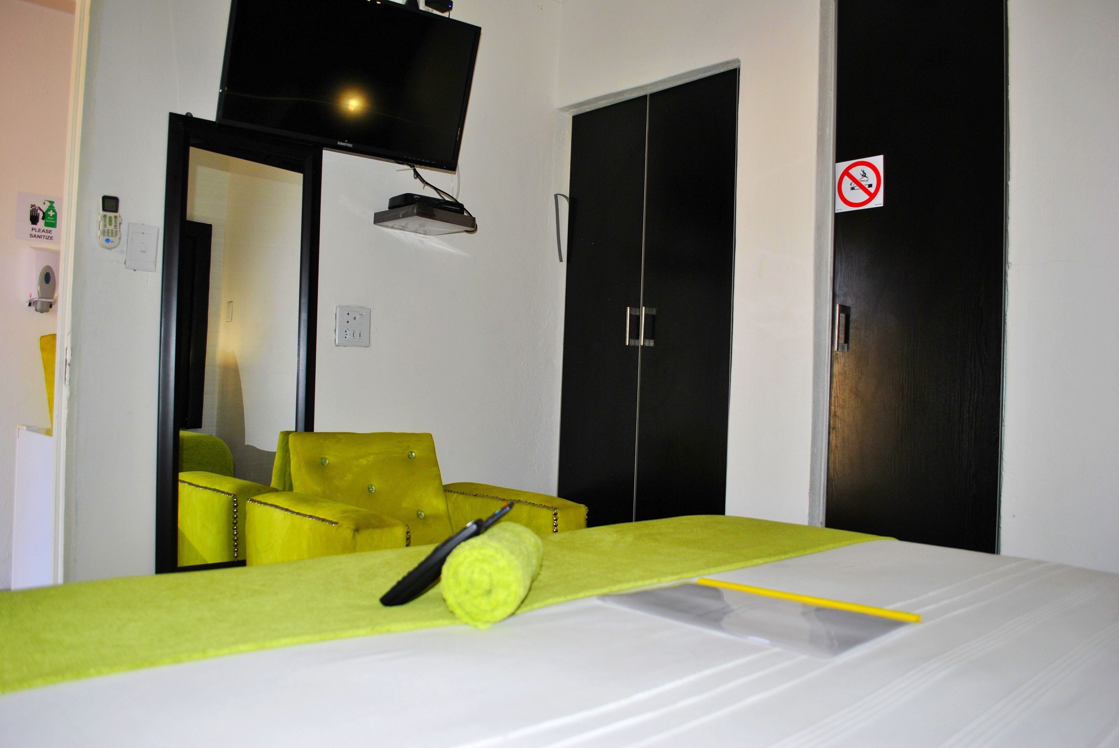 A hotel room with a bed, a yellow armchair, a television mounted on the wall, and a door with a no-smoking sign.