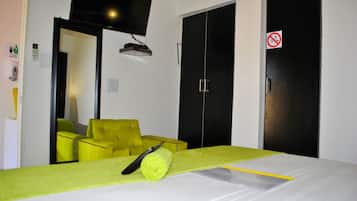 A hotel room with a bed, a yellow armchair, a television mounted on the wall, and a door with a no-smoking sign.